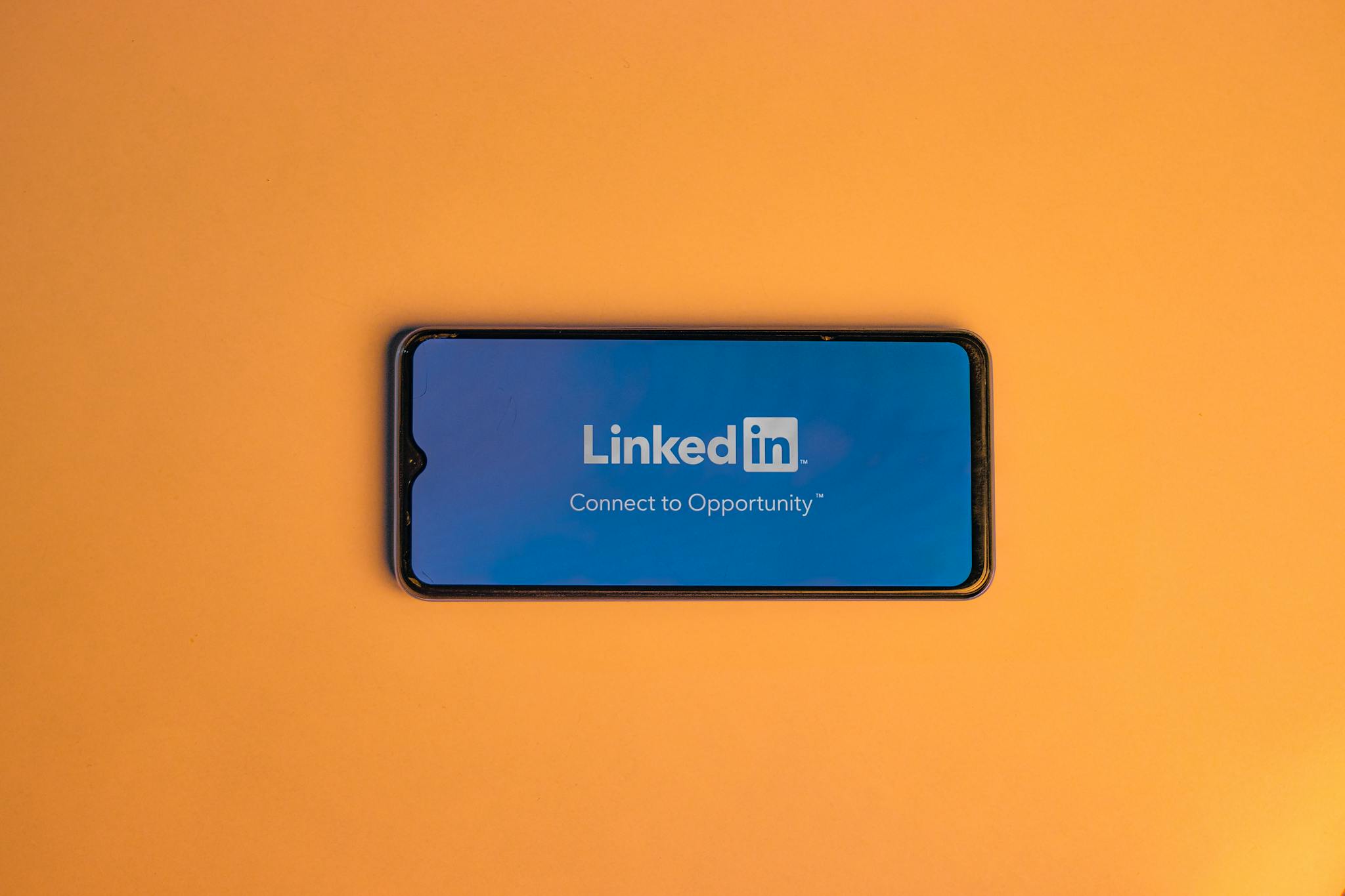 Smartphone showing LinkedIn login on vibrant orange background, symbolizing connectivity.
